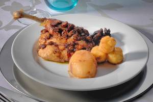 Gebackenes Huhn mit Rosinen und Kartoffeln auf einem weißen Teller.