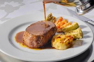 Ein Gericht wird im H10 Estepona Palast serviert, bestehend aus Fleisch, Gemüse und Soße.