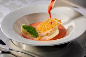 Ein Gericht mit Tomatensuppe in einer weißen Schüssel, serviert mit Minze und geriebenem Käse.
