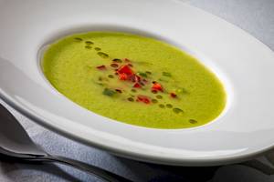 Grüne Suppe in einem weißen Teller mit roten Paprikaschoten und grünem Blatt.
