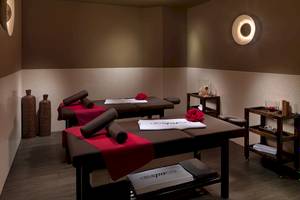 Spa-Behandlungsraum im H10 Estepona Palace Hotel mit zwei Massagetischen, roten Decken, und zwei Rosen.