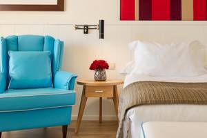 Schlafzimmer im H10 Estepona Palace mit einem Bett, einem blauen Stuhl und einem Nachttisch mit Rosen.