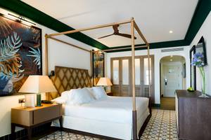 Schlafzimmer im H10 Estepona Palace mit Himmelbett, weißen Laken, zwei Nachttischen und tropischen Wandgemälden.