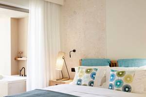Schlafzimmer im Domes Noruz Chania mit weißen Wänden, blauen Kissen und einem weißen Bett.