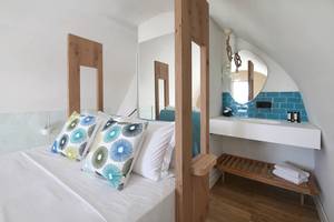 Innenansicht eines Hotelzimmers im Domes Noruz Chania, Autograph Collection, mit einem Bett, blauen Kissen und einem Badezimmerspiegel.