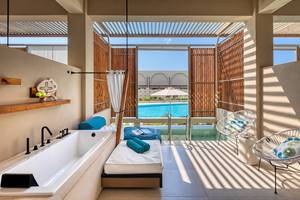 Innenbereich des Domes Noruz Chania, Autograph Collection mit Badewanne, Lounge-Bereich und Pool-Blick.