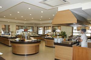 Buffet im Restaurant des Europa Beach Hotel & Spa mit verschiedenen Speisen, serviert von einer Angestellten.