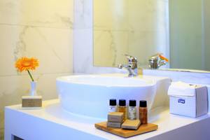 Badezimmer im LABRANDA Marine Aquapark Hotel mit einer weißen Marmorfliesenwand, einem Waschbecken, einer gelben Blume und Pflegeprodukten.