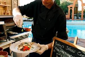 Kochaktion im Orpheas Resort mit Speisen auf einem Teller und einem Mann am Grill.