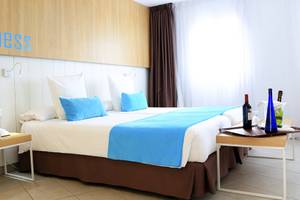 Zimmer im Labranda Playa Bonita Hotel mit zwei Betten, blauen Kissen und einer Tafel mit Weinflaschen.