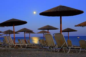 Beim LABRANDA Kiotari Miraluna Resort steht eine Reihe von Sonnenschirmen auf dem Strand bei Mondschein.