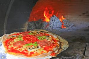 Eine Pizza mit Tomaten, Peperoni und Pilzen brät im Ofen