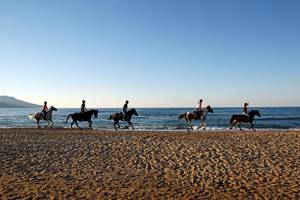 Fünf Menschen reiten Pferde am Strand im Orpheas Resort.