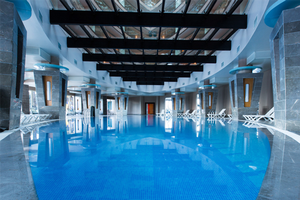 Innenpool des Long Beach Alanya Hotels mit weißen Liegestühlen und einer Glasdecke.