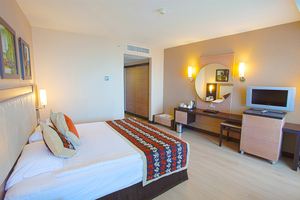 Innenansicht eines Hotelzimmers im Long Beach Alanya Hotel mit Doppelbett, Fernseher, Schreibtisch und Spiegel.