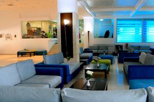 Lobby des Blue Bay Beach Resorts mit blauen Sofas, weißen Wänden und großen Fenstern.