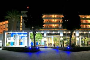 Der Eingang des Blue Bay Beach Resorts in der Nacht mit blauen Lichtern und Bäumen.