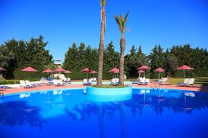 Ein blauer Pool im Blue Bay Beach Resort mit Sonnenliegen und roten Sonnenschirmen.