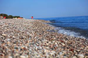 Strand des Blue Bay Beach Resorts mit kleinen Steinen und sanfter Brandung.