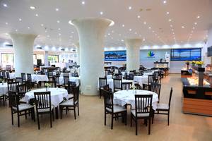 Innenbereich des Blue Bay Beach Resort Restaurants mit runden Tischen und Stühlen, großen Säulen und einer langen Theke.