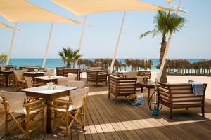 Außenterrasse des Asterias Beach Hotels mit Blick auf das Meer und Palmen.