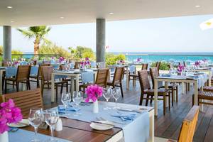 Restaurant des Asterias Beach Hotels mit Blick auf das Meer und gedeckten Tischen.