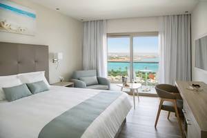 Interieur eines Hotelzimmers im Asterias Beach Hotel mit Blick auf das Meer und eine Terrasse.