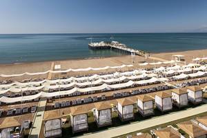 Luftaufnahme des Delphin Imperial Hotels zeigt eine lange Strandlinie mit vielen weißen Sonnenschirmen und Lounge-Stuhlreihen.