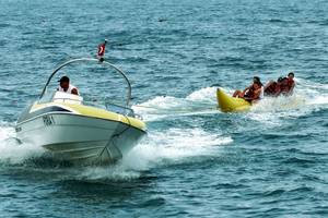 Ein Boot zieht ein Banana Boat mit mehreren Personen im Meer.