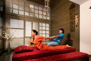Zwei Frauen praktizieren Yoga auf einem roten Bett in einem Hotelzimmer.