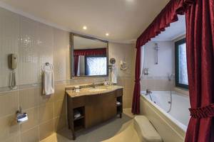Badezimmer des Delphin Palace Hotels mit Badewanne, Spiegel und Waschbecken.