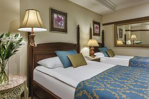 Doppelzimmer im Delphin Palace Hotel mit zwei Betten, Nachttischen, Lampen und Blumenvase.