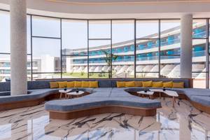 Innenansicht der Lobby im Lyttos Mare Hotel mit geschwungenen Sofas, runden Tischen und großen Fenstern.