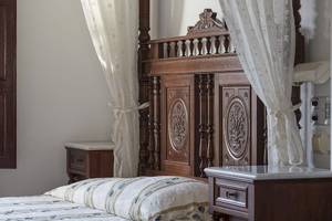 Bett im Veggera Hotel mit kunstvoll geschnitztem Kopfteil und weißen Vorhängen