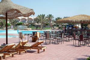 Außenbereich des Three Corners Sea Beach Resorts mit Liegen, Tischen und Sonnenschirmen neben dem Pool.