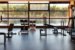 Fitnessraum im Hotel Porto Carras Meliton mit Blick auf den See und Bäumen.