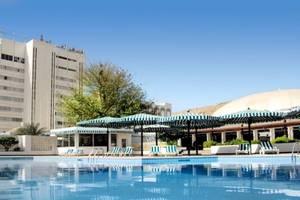 Außenbereich des Al Falaj Hotels mit Swimmingpool, Sonnenliegen und Sonnenschirmen.