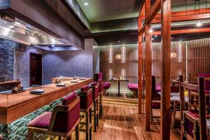 Innenraum des Sushi-Restaurants im InterContinental Muscat mit hölzerner Theke und roten Stühlen.