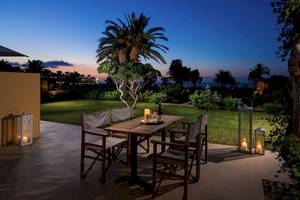 Terrasse mit Tisch und Sesseln im Kernos Beach Hotel bei Sonnenuntergang.