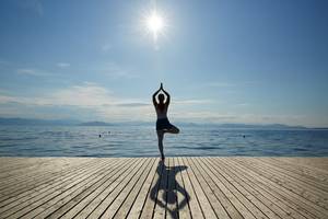 Eine Person praktiziert Yoga in einer Balance-Pose auf einer Holzplattform am Meer.