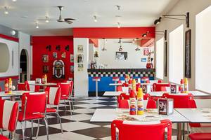 Innenraum des Restaurants im MarBella Corfu Hotel mit rotem und weißem Thema, schwarzen Fliesen und rot-weißen Stühlen.