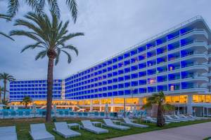 Außenansicht des Vibra Algarb Hotels mit blau beleuchteten Fenstern und Loungestühlen im Freien.