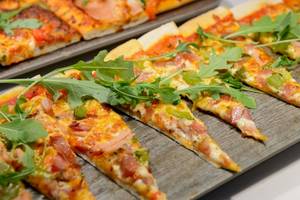 Mehrere Scheiben einer pikanten Pizza auf einem hölzernen Brett.