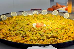 Großer Teller mit Paella, gefüllt mit Reis, Gemüse und Fleisch, dekoriert mit Zitronenscheiben.