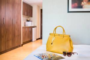 Gelbe Lederhandtasche auf einem Bett mit einer Brille und einer Zeitschrift
