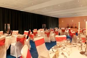 Bankettsaal im Park Plaza County Hall London mit gedeckten Tischen, Kerzen und roten Schleifen.