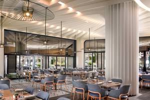 Innenansicht des Restaurants im Khalidiya Palace Rayhaan by Rotana mit modernen Möbeln und Glaswänden.
