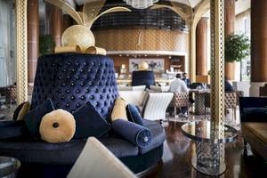Loungebereich im Khalidiya Palace Rayhaan by Rotana mit blauen und goldenen Kissen, einem runden Tisch und goldenen Wanddekorationen.