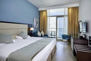 Innenansicht eines Hotelzimmers im Riu Dubai mit Doppelbett, Sofa, Fernseher und Meerblick.