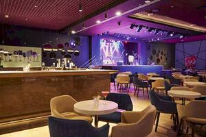 Innenansicht der Bar im Riu Dubai Hotel mit Tisch, Stühlen und einer Bühne.